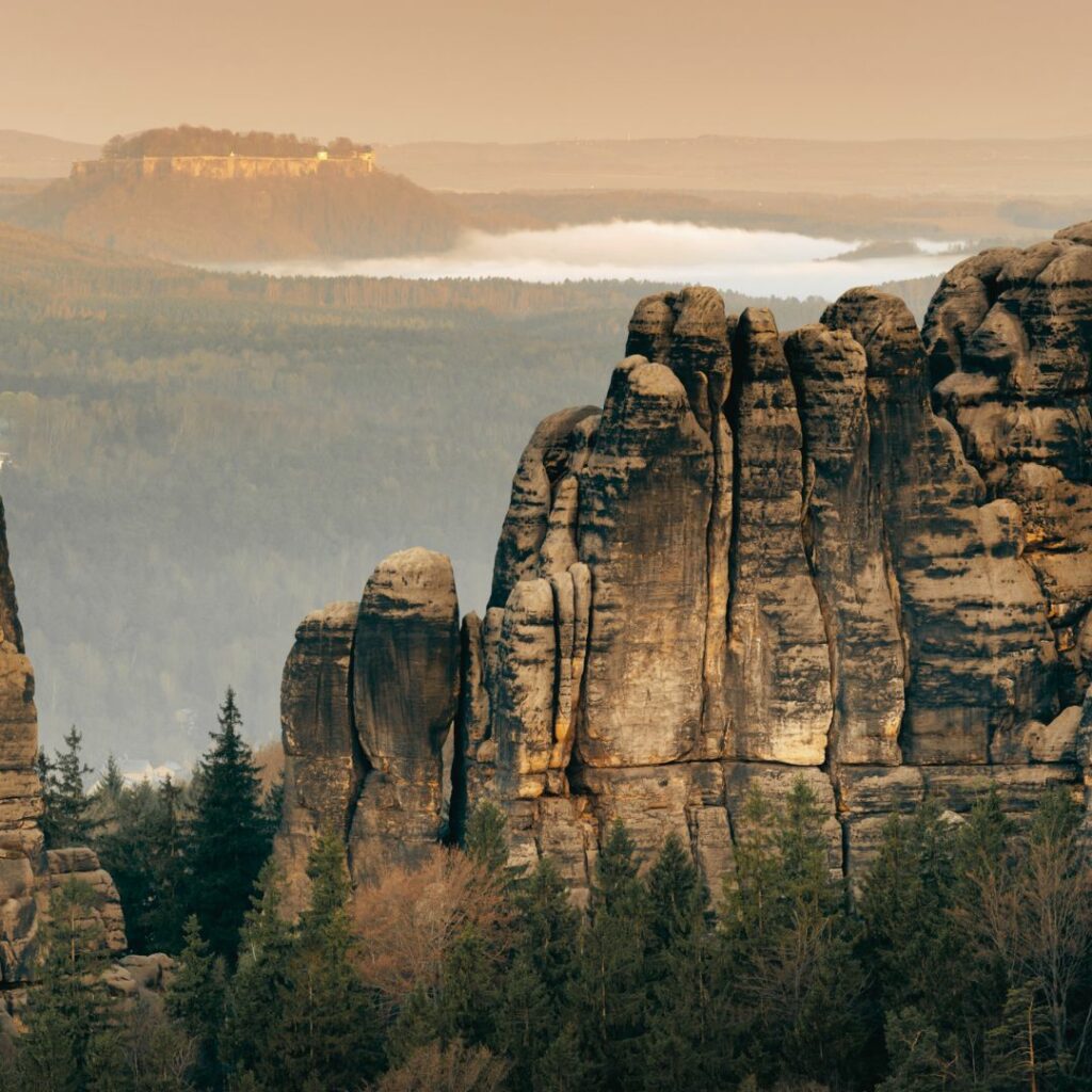 Zu sehen sind die beeindruckenden Felsformationen, die in den Himmel ragen. Sie sind von einem Nadelwald umgeben und im Hintergrund sieht man weiteren Wald, Hügel und Felsen. 