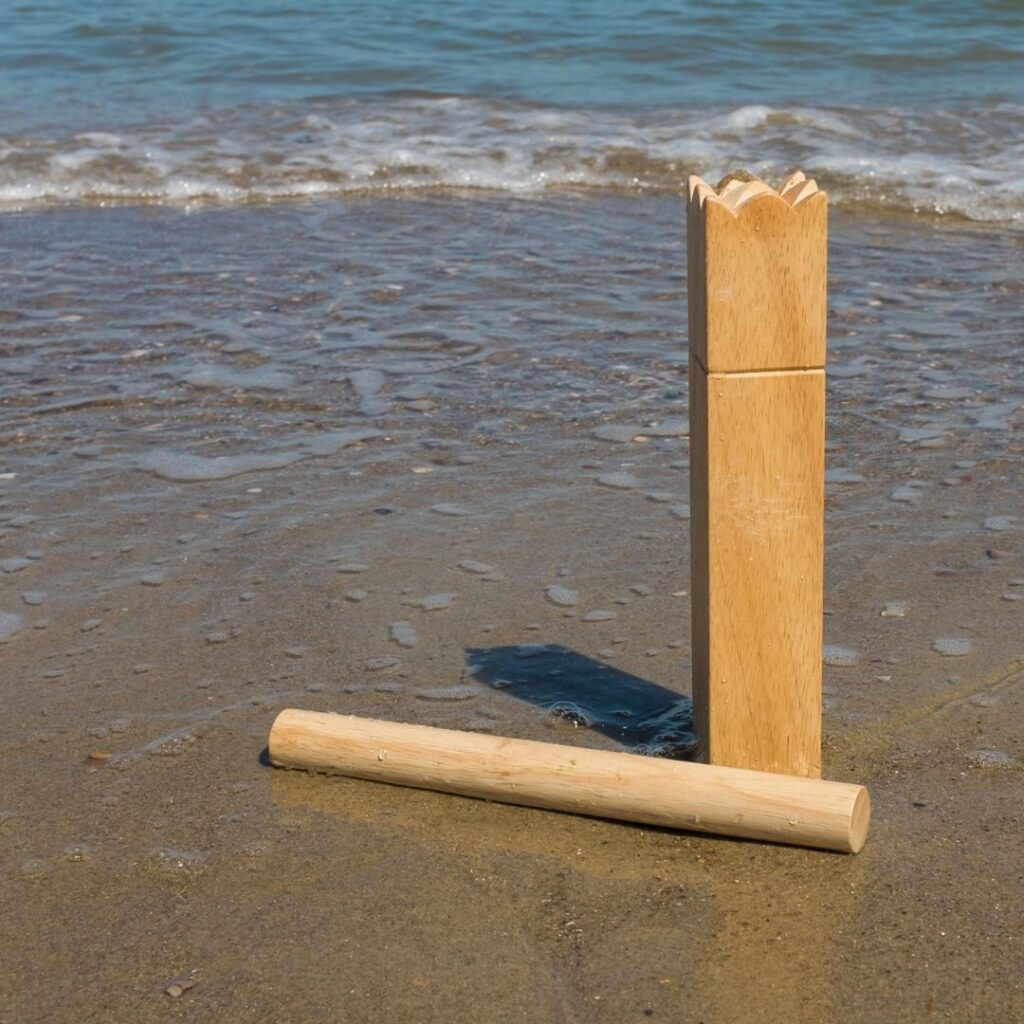 Zwei Holzklötze des skandinavischen Spiels Kubb stehen auf dem Strand im nassen Sand. Im Hintergrund sieht man ruhige Wellen des Meeres. 