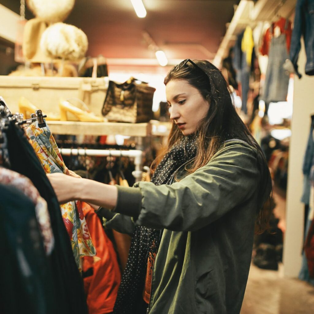 Eine junge Frau sucht in einem Second-Hand-Laden nach Klamotten.